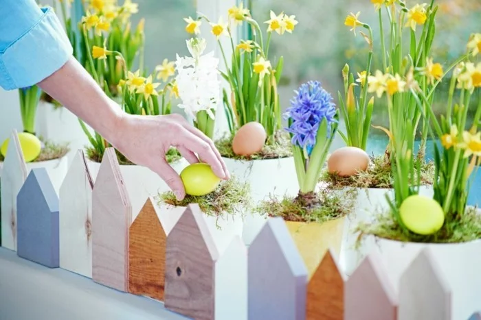 Osterdeko Fenster mit mehreren Blumen und Eiern mit hölzernen Häusern umrahmt
