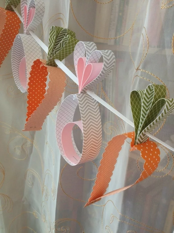 Möhren aus Bastelpapier in verschiedenen Farben auf eine Schnur als Girlande geordnet