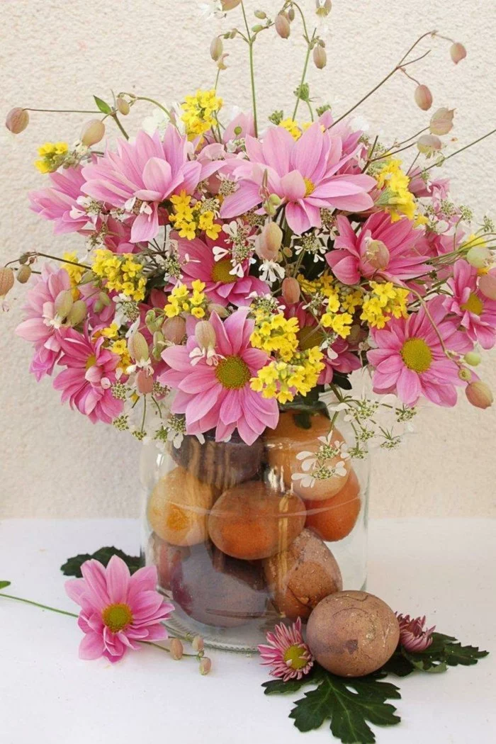 Eier und Blumen in einem Glasgefäß arrangieren 