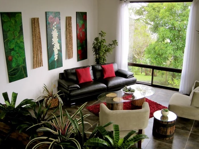Grünpflanzen, Wandbilder, schwarzes Ledersofa und rote Dekokissen