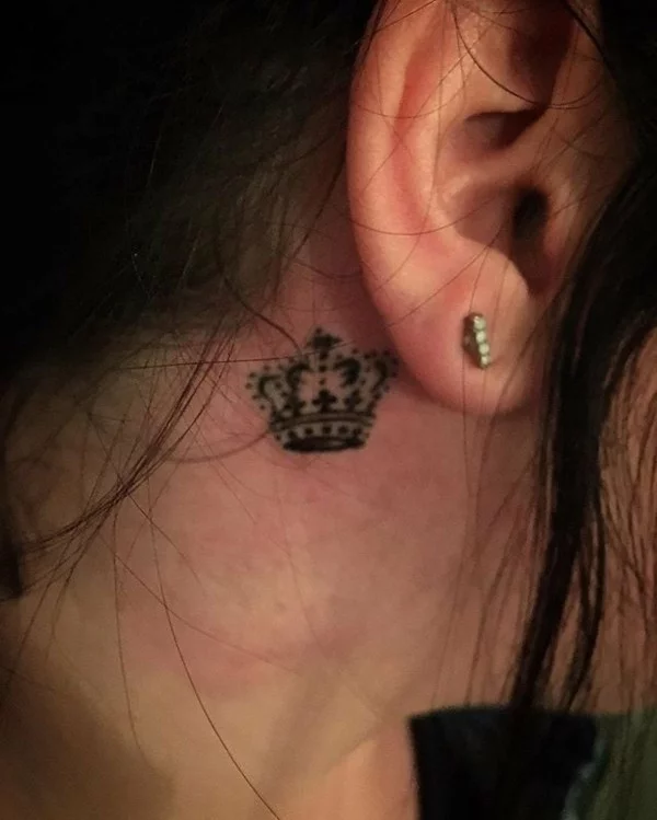 kleines Tattoo mit Krone hinter dem Ohr 