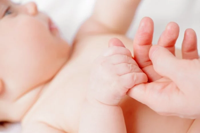 Sweet three-month-old baby is holding her mother's hands. Parent