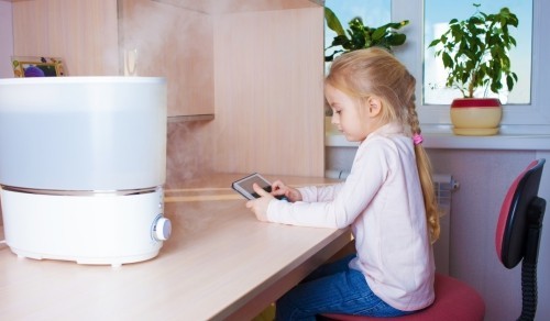 Little girl with tablet pc sitting at the table near humidifier
