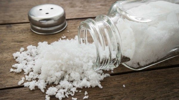 Spilled salt with salt shaker on wooden background