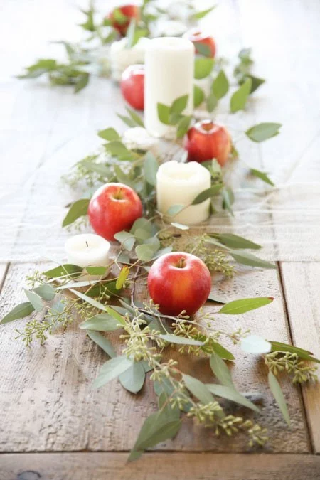 Tischdeko im Herbst rote Äpfel Kerzen grüne Blätter