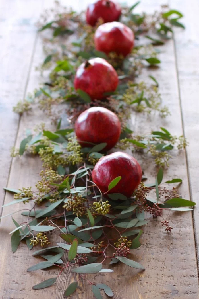 Tischdeko Ideen zu Weihnachten Granatäpfel und grüne Blätter zum Dekorieren