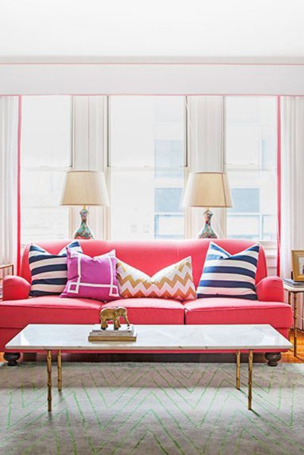Wohnaccessoires im modernen Wohnzimmer rosafarbenes Sofa bunte Deko Kissen Lampen Statuette aus Bronze