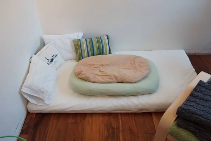kleines Montessori Bett mit weißer Bettwäsche und bunten Kissen 