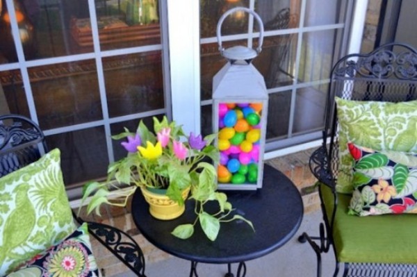 Osterdeko draußen Terrasse dekorieren bunte Sitzkissen Laterne mit bunten Eiern Topf mit Grünpflanze und Blumen darin