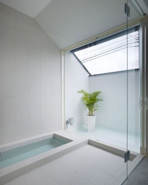 Eingelassene Badewanne minimalistisch gestaltet weiß dominiert Bergpalme als Akzent