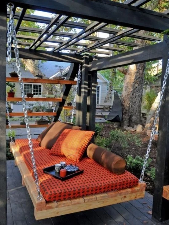 Hängebett draußen im Garten orangenfarbene Polsterung ein Tablett mit Kaffeetassen Kerze darauf