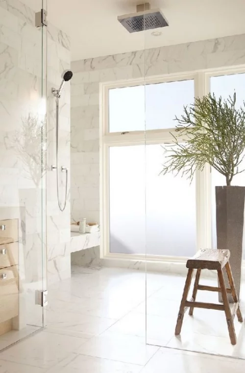 schönes Baddesign heller Marmor im Bad in Beige Glaswand Holzhocker Pflanze viel Licht