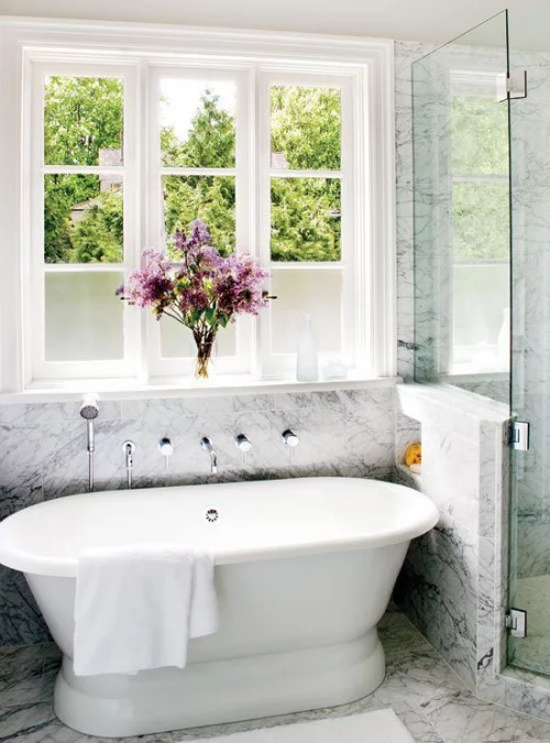 Marmorfliesen weiße Badewanne vor dem Fenster Vase mit Blumen feminines Flair Marmor im Bad 