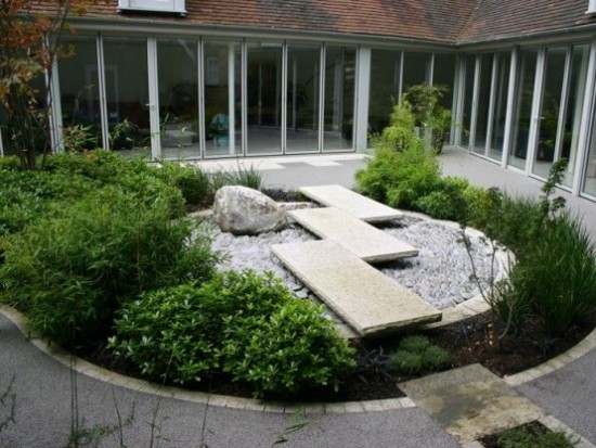 Japanischer Garten im Hinterhof runde Form Steinplatten Felsbrocken Kiesel grüne Sträucher