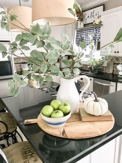 Herbstdeko in der Küche auf einem runden Holzbrett Kürbis Buch Schale mit Äpfeln weiße Porzellankanne mit Eukalyptuszweigen