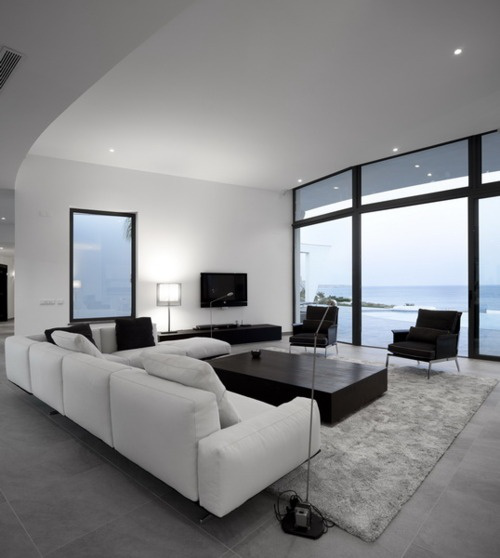 Minimalismus im Wohnzimmer großer Raum schöner Ausblick weißes Ecksofa grauer Teppich niedriger Tisch in Schwarz