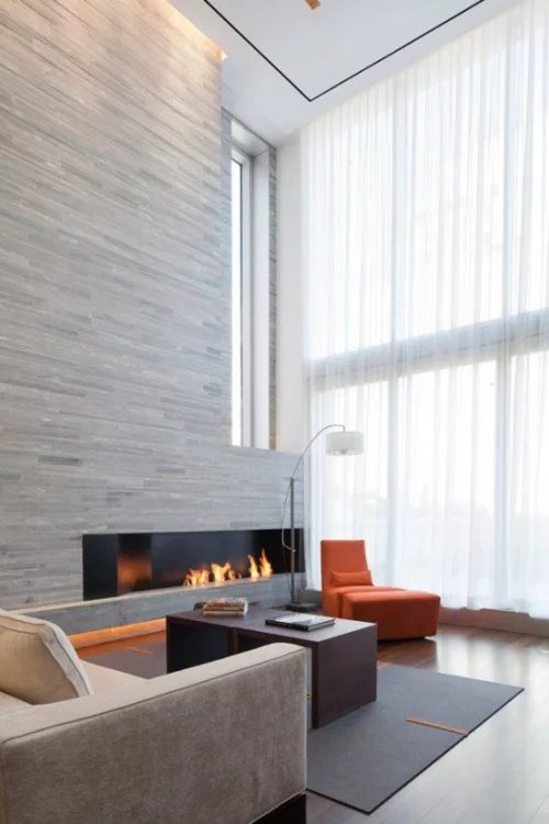 Minimalismus im Wohnzimmer hoher Raum hellgraue Farbgestaltung moderner Sessel in Orange am Fenster Blickfang