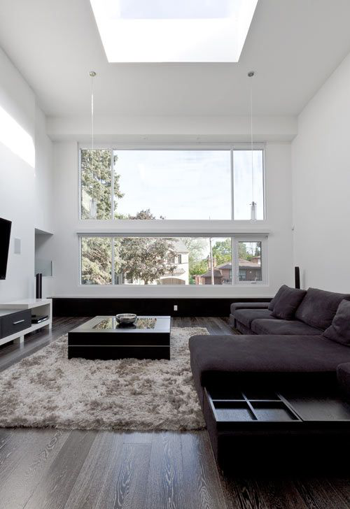 Minimalismus im Wohnzimmer perfektes Design dunkles Ecksofa Teppich Fernsehwand großes Fenster viel Tageslicht