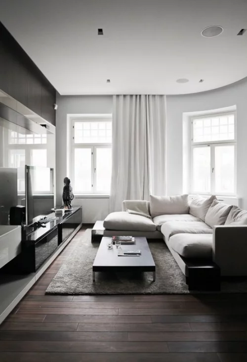 Minimalismus im Wohnzimmer perfektes Design weiße Sitzgarnitur grauer Teppich schwarzer Tisch graue Gardinen