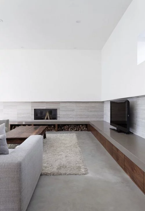 Minimalismus im Wohnzimmer perfektes Raumdesign eingebauter Kamin Brennholz Fernseher graues Sofa Teppich