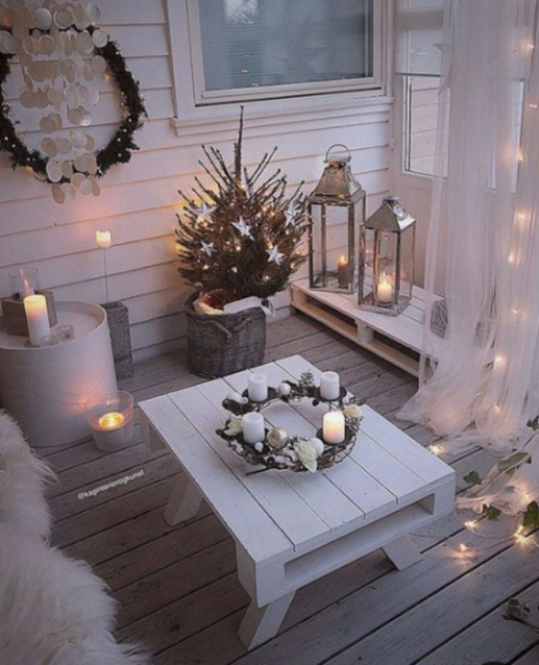 Weihnachtsdeko für Balkon ganz in Weiß zahlreiche Lichter und Kerzen Adventskranz auf einem niedrigen weißen Tisch in der Mitte