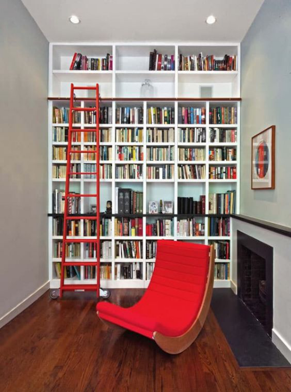 Moderne Hausbibliothek Kamin roter Schaukelstuhl Bücherwand deckenhoch Leiter