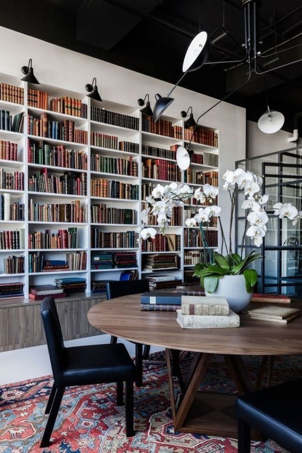 Moderne Hausbibliothek runder Tisch Sitzgelegenheiten weiße orchideen passendes Licht
