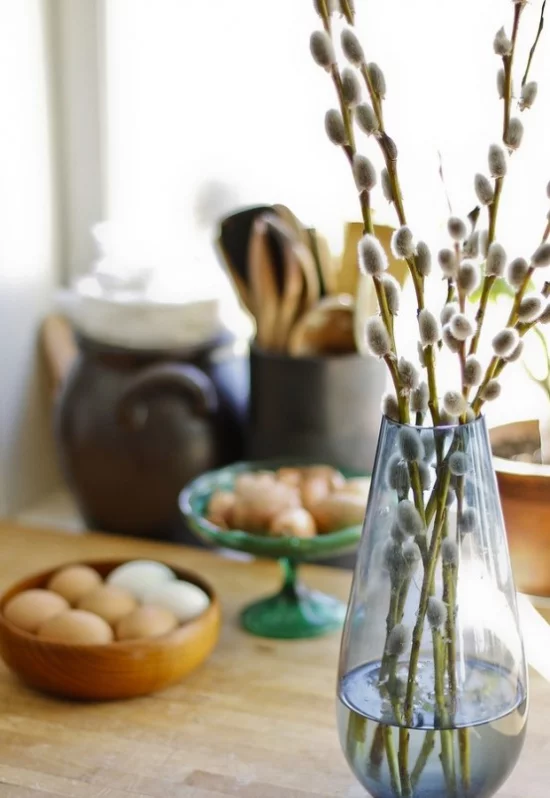 Frühlingsdeko mit Weidenkätzchen in Glasvase arrangiert Eier im Hintergrund