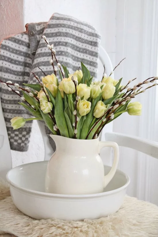 Frühlingsdeko mit Weidenkätzchen in weißer Porzellankanne mit gelben Tulpen arrangiert