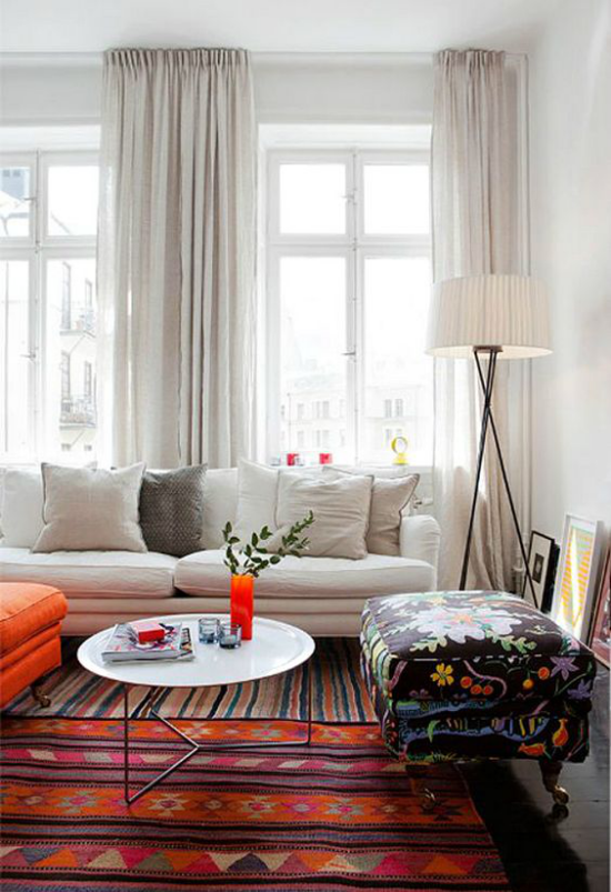 Wohnzimmer optisch erweitern weißes Sofa weiße Gardinen viel Tageslicht bunter Teppich Orange dominiert