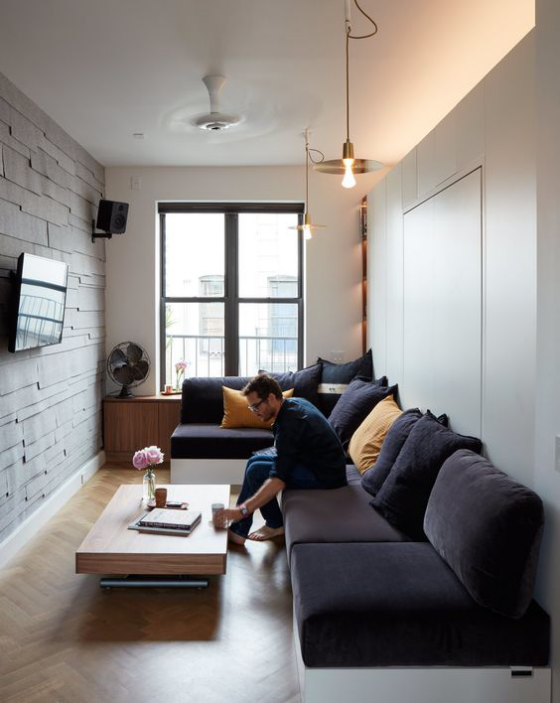 Zeitgemäße Raumgestaltung modernes enges Wohnzimmer dunkellila Ecksofa Fernseher an der Ziegelwand