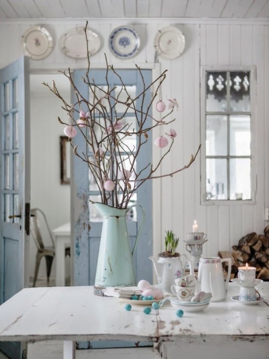 Osterdeko in Pastellfarben im rustikalen Stil Tisch ländlich dekoriert Gießkanne mit Zweigen und Pompons