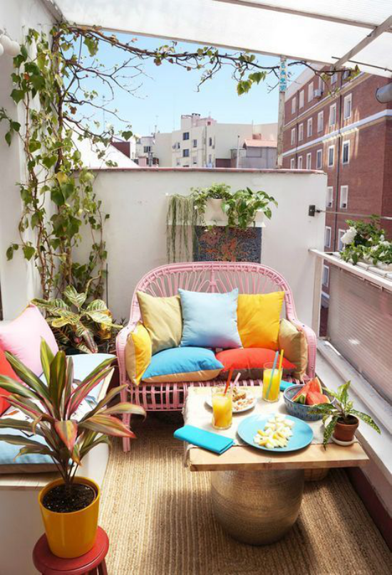 Terrasse frühlingsfit machen kleinen Balkon gestalten kleine Sofas runder Tisch viele Blumen bunte Kissen frühlingshafte Stimmung