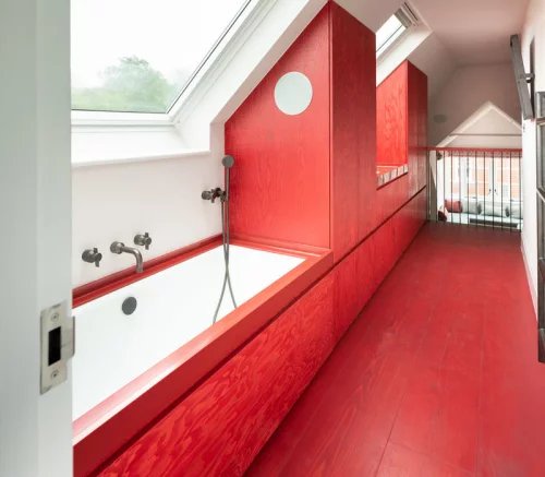 Badezimmer in Rot unter der Schräge viel Tageslicht rote Vertäfelung Badewanne unter dem Dachfenster rote Schränke