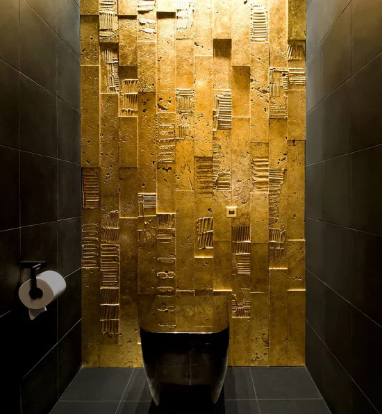 Badezimmer in Schwarz und Gold WC eine Wand in Goldschimmer interessante Oberfläche andere zwei Wände Boden und Toilettenschüssel schwarz