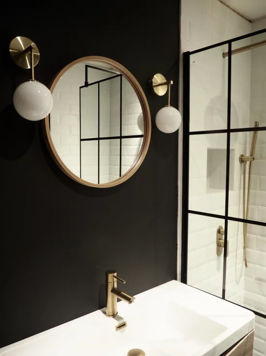 Badezimmer in Schwarz und Gold das Farbschema durchbrechen Weiß Spiegel goldener Rahmen zwei Hängelampen Armatur in Gold