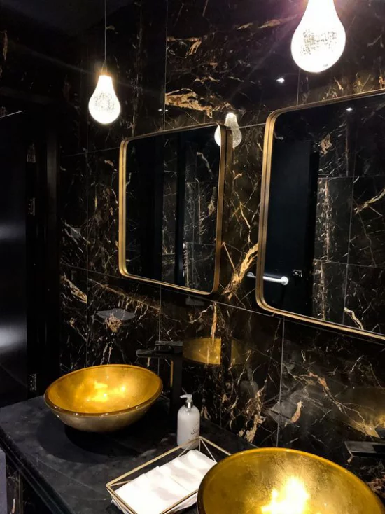 Badezimmer in Schwarz und Gold doppelter Waschtisch runde Waschbecken schwarze Marmorfliesen zwei Spiegel vergoldete Rahmen