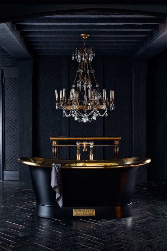 Badezimmer in Schwarz und Gold dunkles Ambiente freistehende Badewanne goldglänzende Elemente luxuriöser Kronleuchter darüber