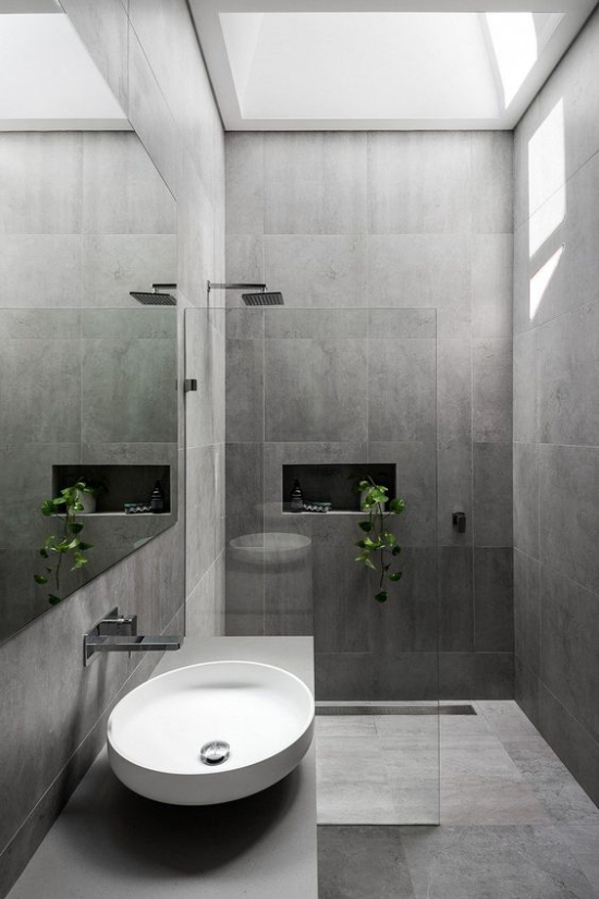 Baddesigns in Grau große Fliesen weißes rundes Waschbecken Duschecke Glaswand Tageslicht von oben grüne Badpflanze