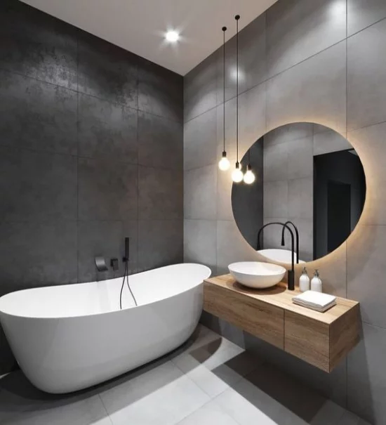 Baddesigns in Grau große graue Wandfliesenweiße Badewanne Hängelampen eingebautes Deckenlicht Waschtisch Holz runder Spiegel