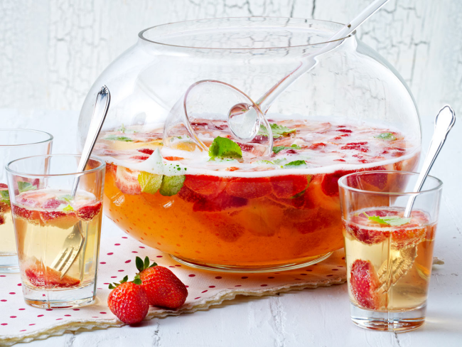 Sommerbowle zubereiten frisch lecker fruchtig Erdbeeren Saft Blätter frische Minze in Glasschale Gläser