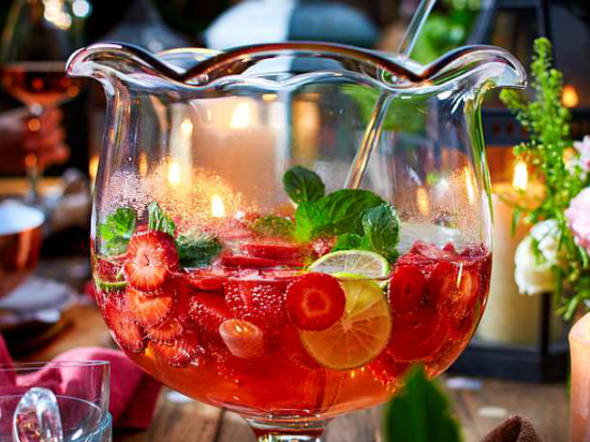 Sommerbowle zubereiten frisch lecker fruchtig Erdbeeren Saft Blätter frische Minze in Glasschale zwei Gläser