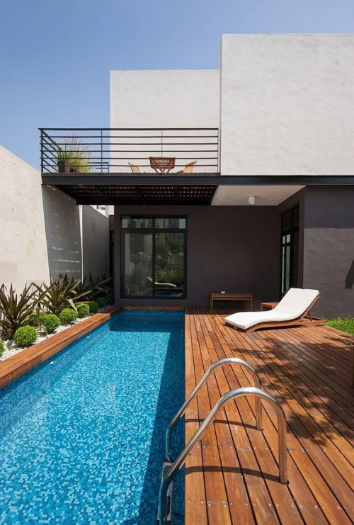 Schmale Pools auf wenig Platz für kleine Gärten Deck aus Holz Pool-Treppe aus Metall moderne Relax Liege rechts grüne Pflanzen links