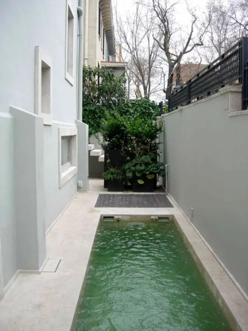 Schmale Pools auf wenig Platz für kleine Gärten begrenzte Fläche zwischen Betonzaun Hausseite grüne Sträucher im Hintergrund