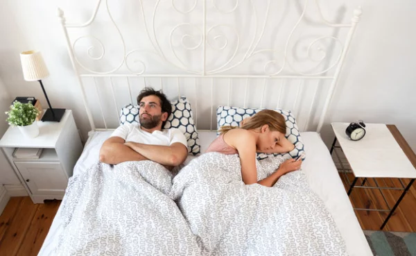 drei Sternzeichen junges Paar im Bett Mann im Zweifel Frau mit Handy in der Hand