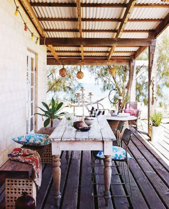 Boho Style Veranda Boden aus Holzplatten Holztisch Sitzbank aus Holz alte Metallstühle grüne Pflanzen Sitzkissen