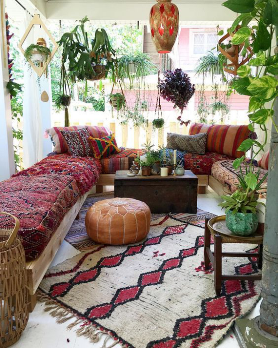 Boho Style Veranda Teppich in grauweiß und Weinrot Sofa bunte Decke viele grüne Pflanzen Hängelampe