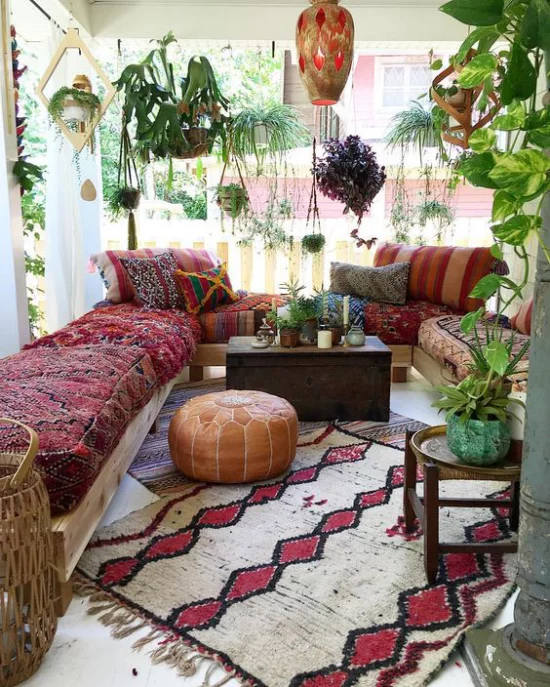 Boho Style Veranda Teppich in grauweiß und Weinrot Sofa bunte Decke viele grüne Pflanzen Hängelampe