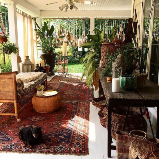 Boho Style Veranda sehr stilvoll einladend Perser Teppich in Dunkelrot viele üppige Grünpflanzen Holz Rattan Hund