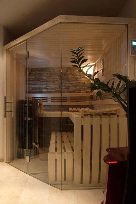 Sauna zuhause saunieren Steinwand Bänke aus Holz hinter Glaswand schickes Design
